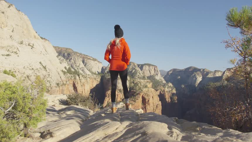 A tall woman stands before a mountain range where she looks out into the distance