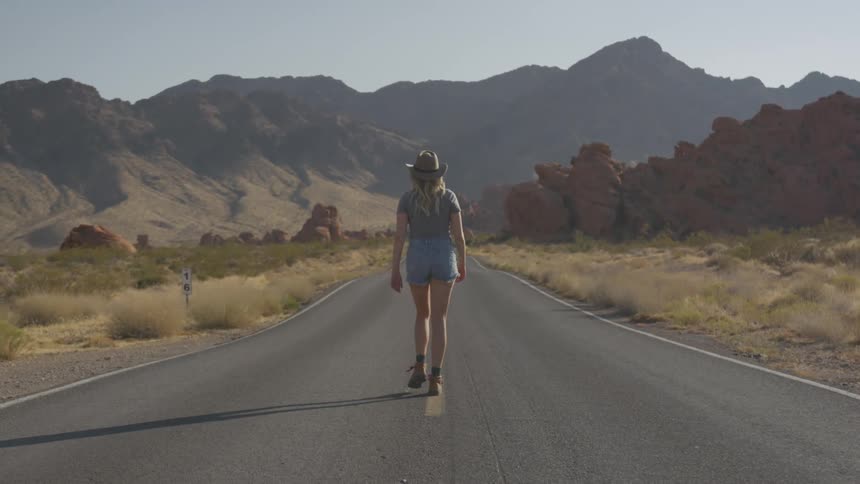 A woman walks in the middle of a deserted road in a desert rural setting