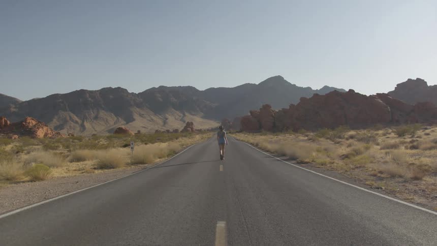 A female walking down the middle of the road with grasslands on either side of her