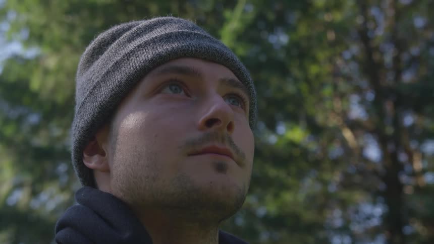 A man with a hat standing with trees and the sky in the background