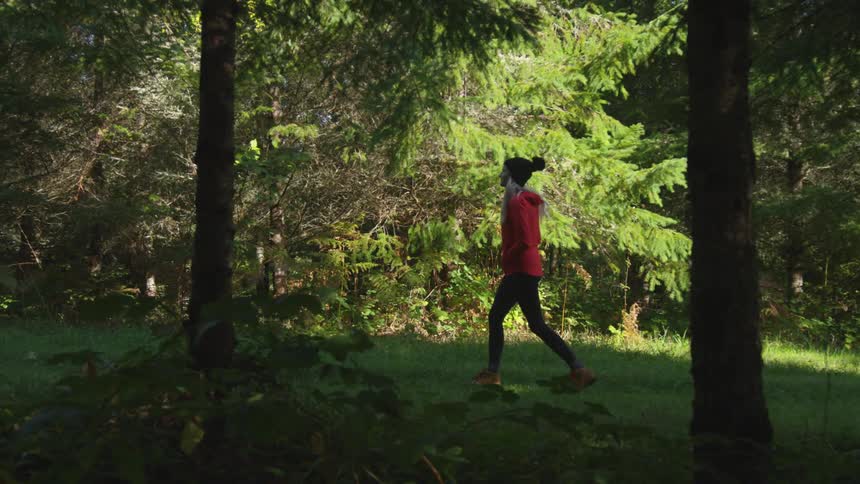 Woman moves through shadows over mowed grass among trees