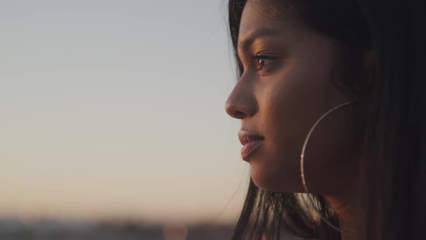 Young woman wearing big metallic round earrings looks at the sunset pensively
