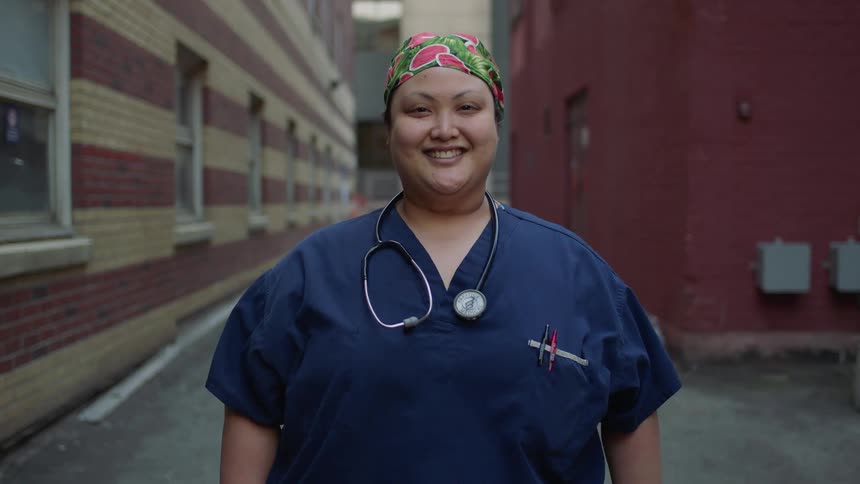 A nurse stands outside and takes her mask off