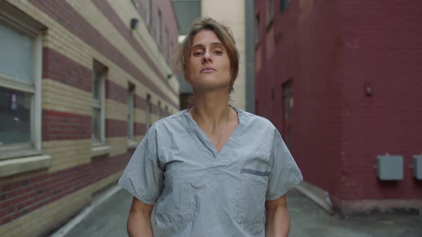 Female nurse demonstrates how to take off a face mask and then smiling happily in the alley