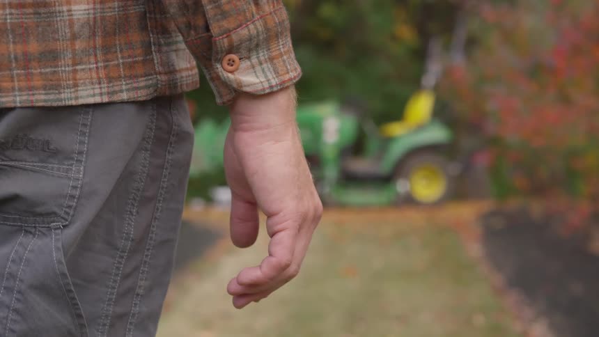 Man stands on a garden looking at a riding lawn mower on a garden