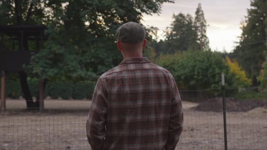 A man stands and looks at a fenced off area of land in a rural area