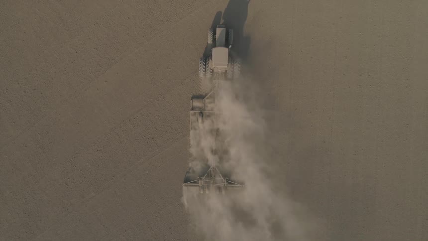 Tractor pulling plow is coated in dust being kicked up