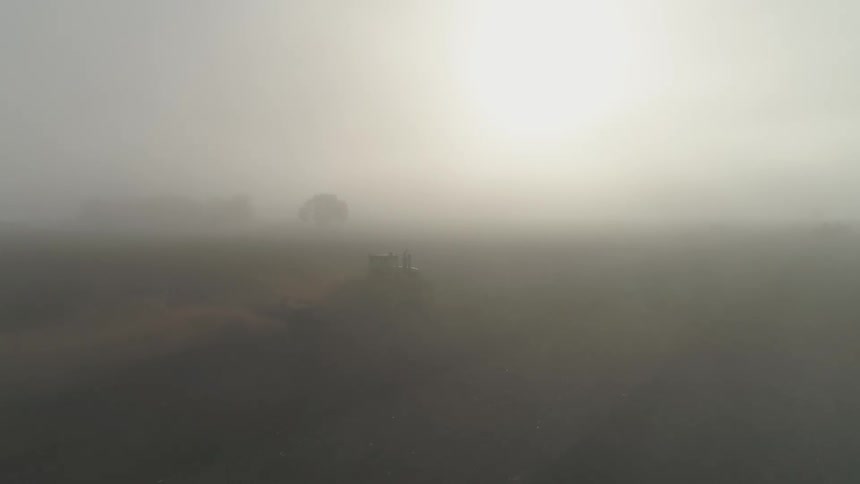 Aerial view of a tractor pulling a sowing machine over the soil in a farm