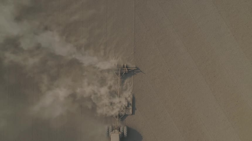 Top down aerial view of a tractor pulling a sowing machine on the a dusty field