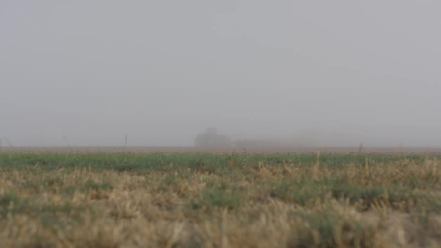 A farm vehicle works the field in the distant fog