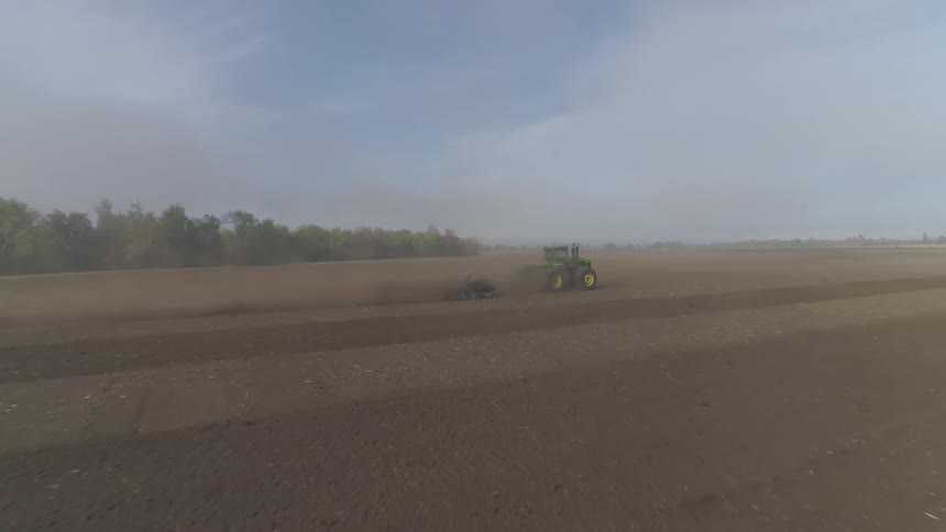 A tractor pulls a plow through a field of dirt on a sunny day