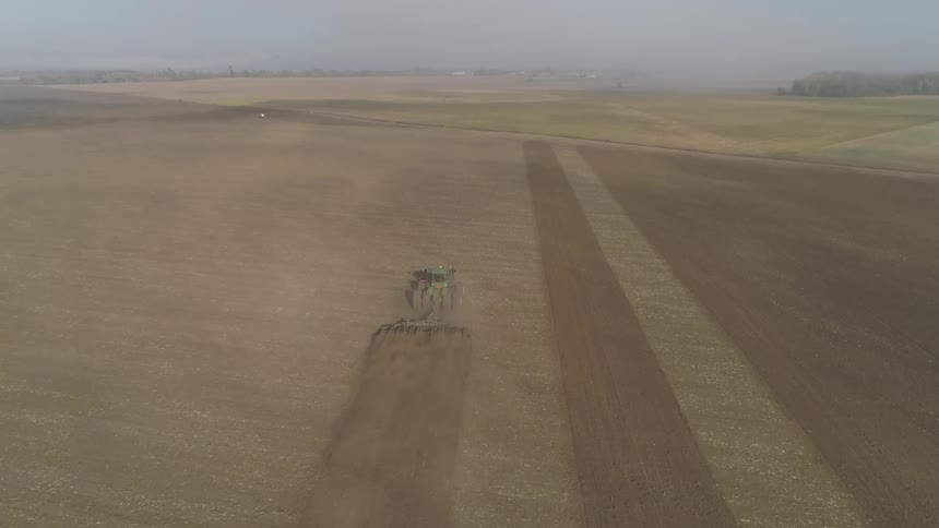 Tractor pulling a sowing machine on a field in a farm