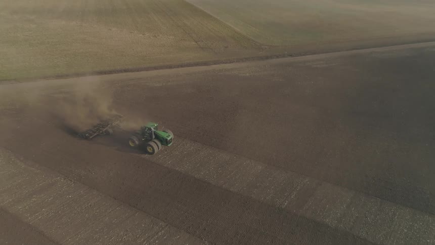 Dust billows behind a tractor as it moves across a large field