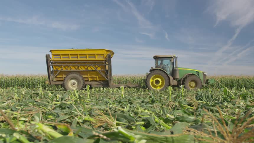 Green tractor pulling a cart through a corn field