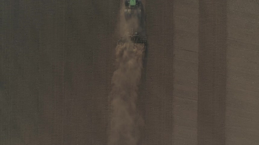 Aerial top down view of a tractor pulling a sewing machine on a cloud of dust in the field