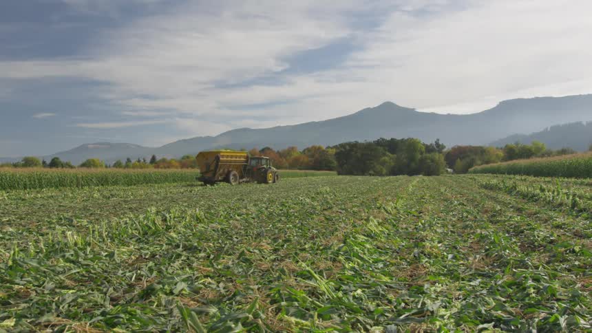 Tractor drives through field in front of mountain range