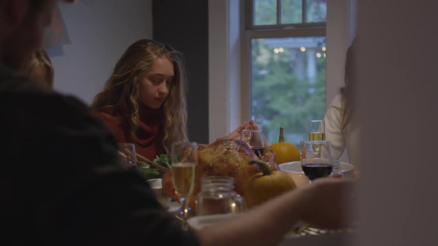 People sitting around the table with a meal and wine hold hands and pray