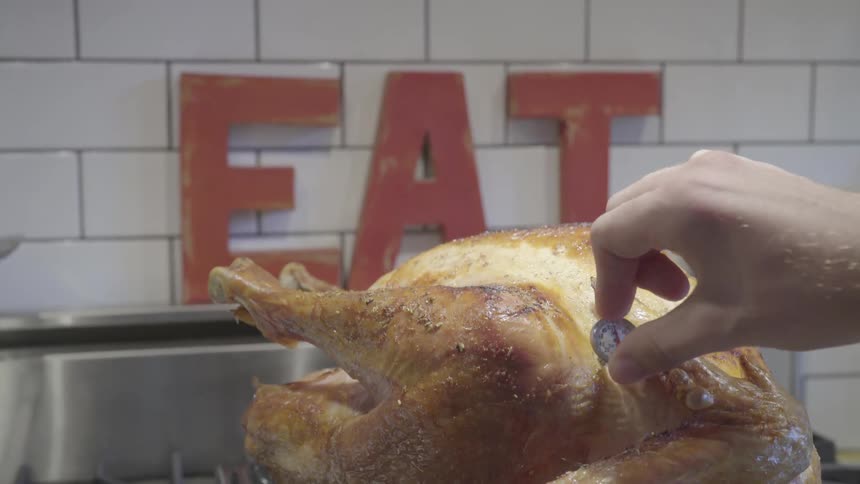 Person inserts thermometer in roasted turkey near letters spelling the word eat