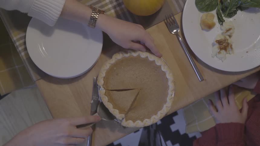A person cuts a piece of pumpkin pie and transfers it to a plate