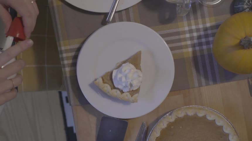 Person sprays whipped topping onto pumpkin pie