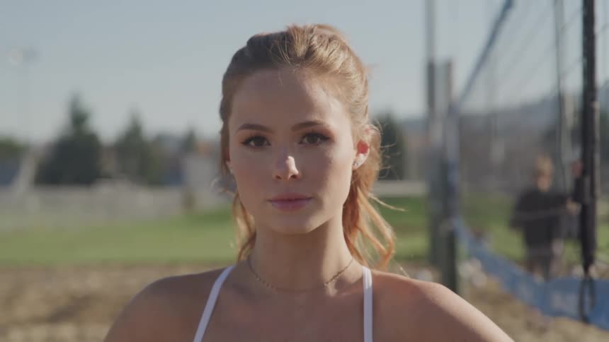 Woman stands next to a fence as someone tosses a ball behind her