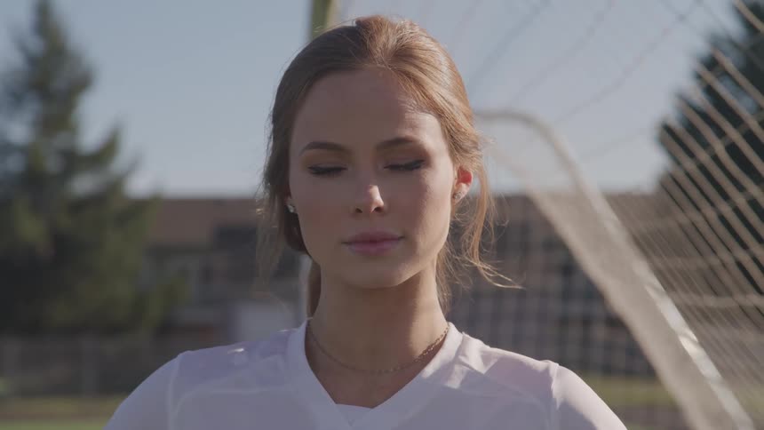 A teenage girl stands in a goalie net on a soccer field