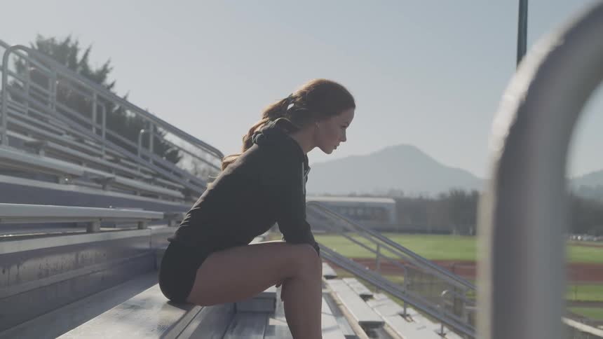 A woman sitting on bleachers with trees a mountain range and the sky in the background
