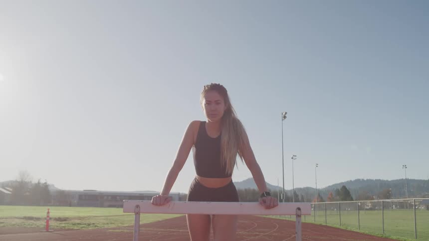 Young woman in sports clothes reclines on an hurdle in the race track