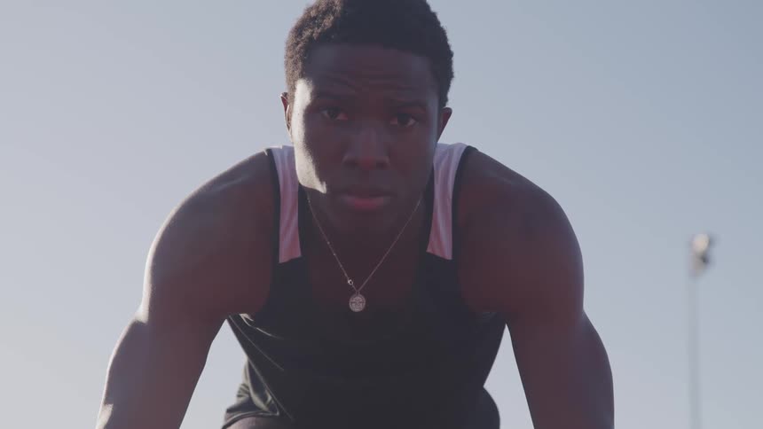 A young black man poses as he prepares to begin running on a track