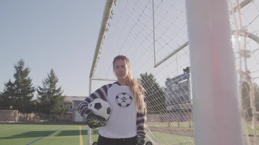 Female athlete stands near soccer goal holding soccer ball