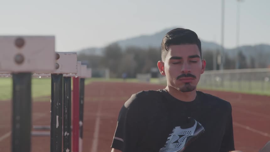 A hispanic man in a black shirt sits on a empty track staring ahead