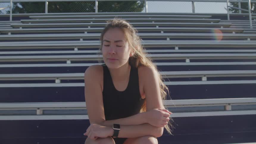 Young woman wearing sports clothes sits on the steps of a stadium at sunset