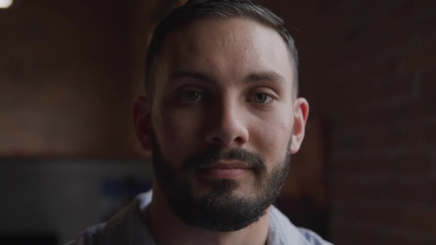 A young man with a beard is near a brick wall