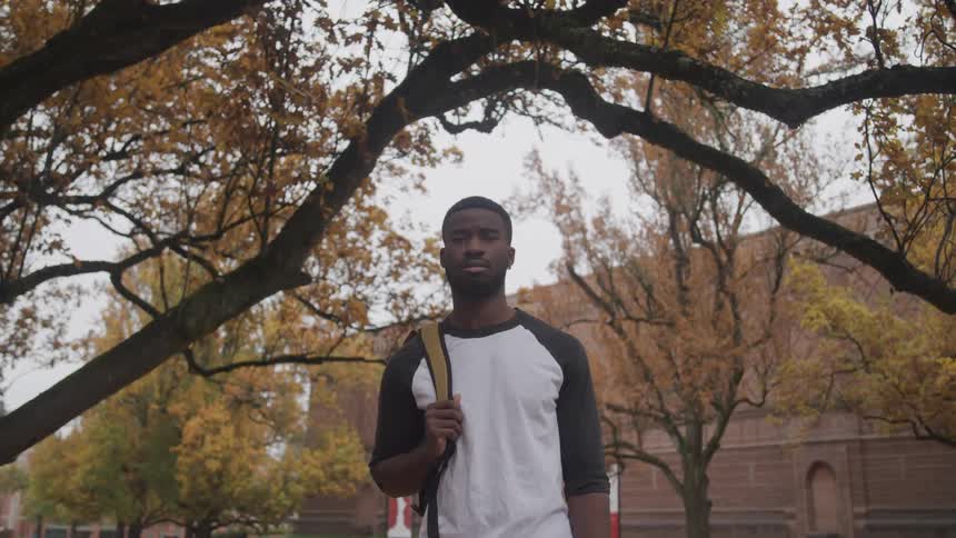 A male college student stands outside the campus building with his backpack