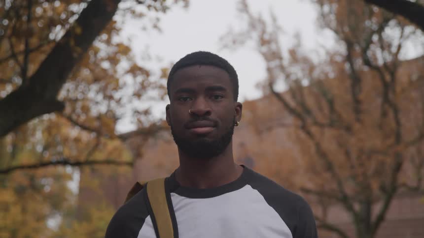 A young black man standing outside a building under trees