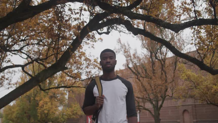 A man with a backpack standing with trees and a building in the background