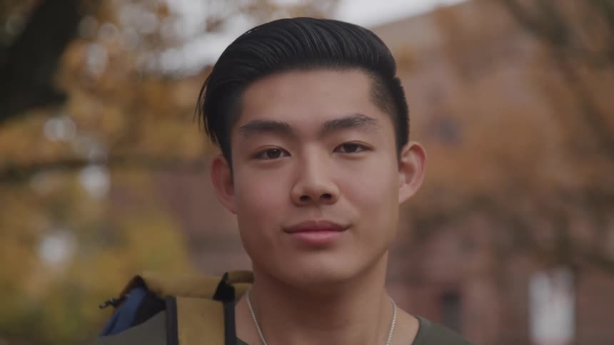 Young man with a backpack looking at the camera while standing outdoors near the trees