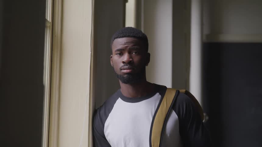 Black man with a beard and a yellow backpack over his shoulder looks at the camera with eye contact