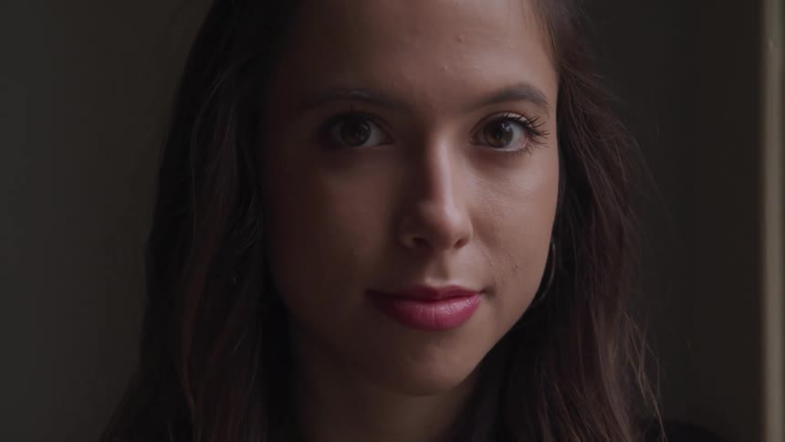 A woman with lipstick standing and staring with a wall in the background
