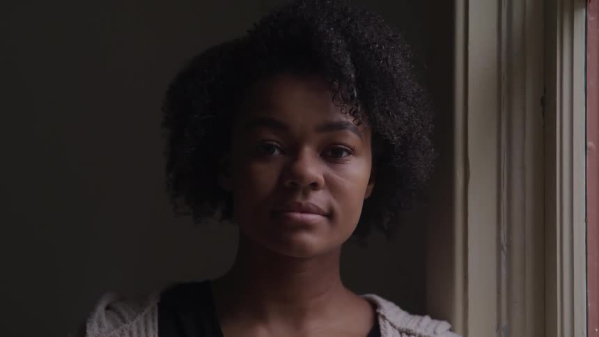 Woman looking out the window in a room turns her face to the camera