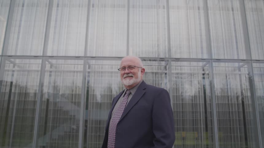 Senior citizen wearing a suit and necktie stands in front of a building looking at the camera