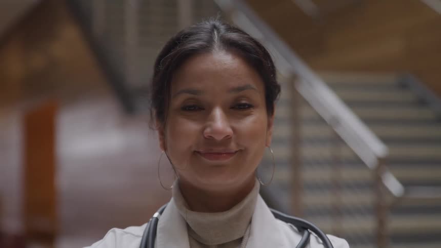 A doctor stands stands by a staircase and smiles