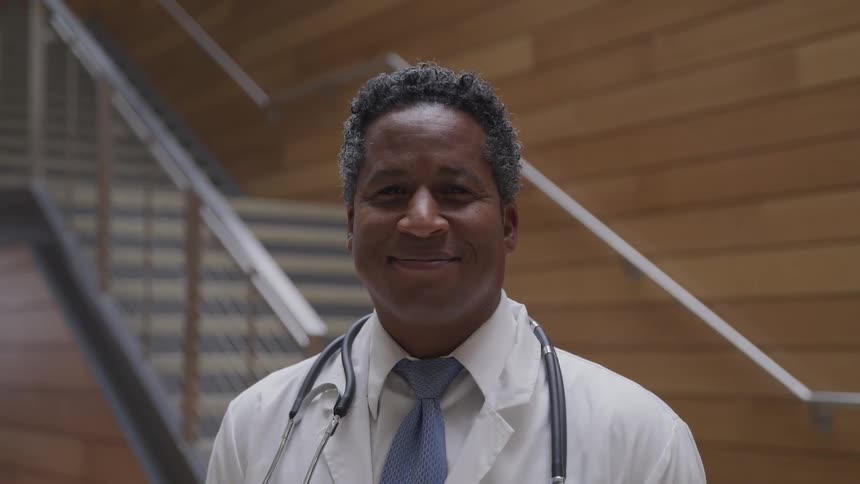 A doctor is standing in a building and is smiling