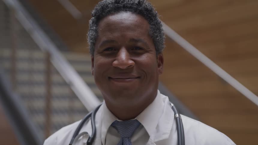 A doctor smiles as he stands at the bottom of a set of stairs