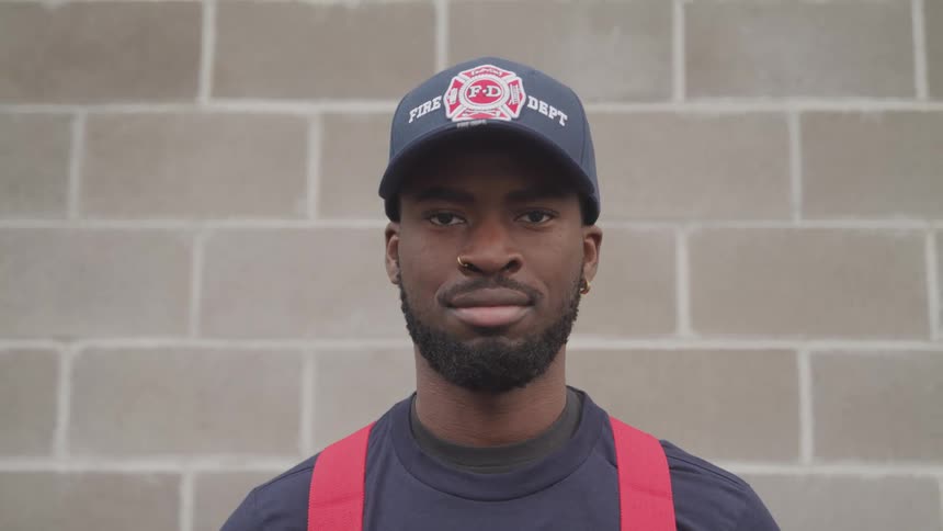 Young firefighter wearing a baseball hat looks at the camera while standing outdoors