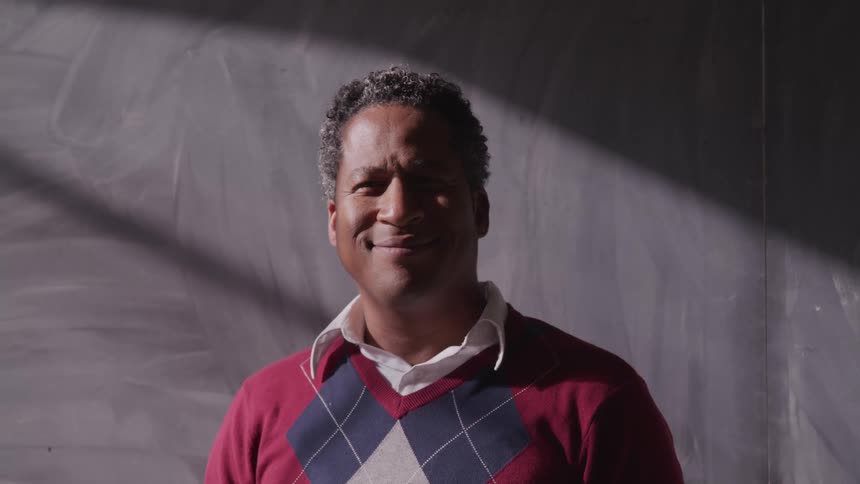 Male teacher in front of chalkboard smiling