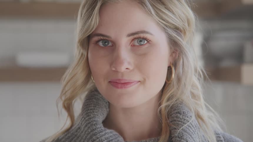 A young woman with blonde hair looks straight forward at the camera as she poses