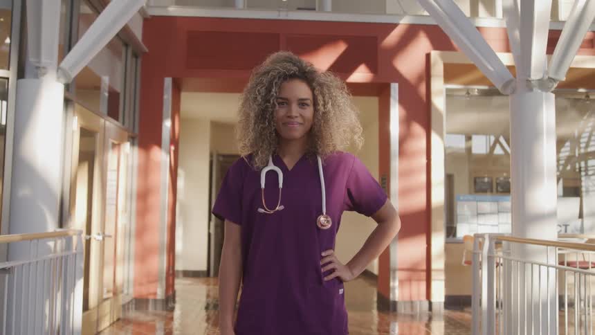 A young black woman wearing scrubs poses with a stethoscope draped over the back of her neck