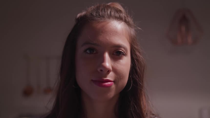 A woman with lipstick standing and staring with a wall in the background