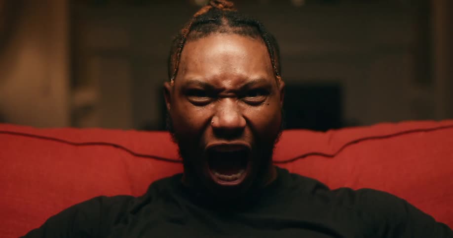 A man sitting on a couch opens his mouth and starts screaming
